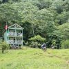 A group of people hiking and swimming near a small house on a hillside.